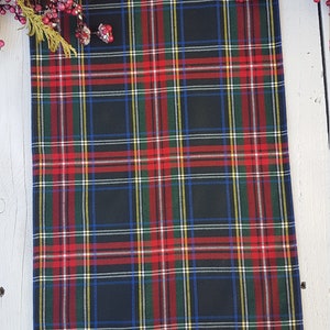 May include: Black and red plaid fabric with a green, white, and blue plaid pattern. The fabric is folded and lying on a white wooden surface.