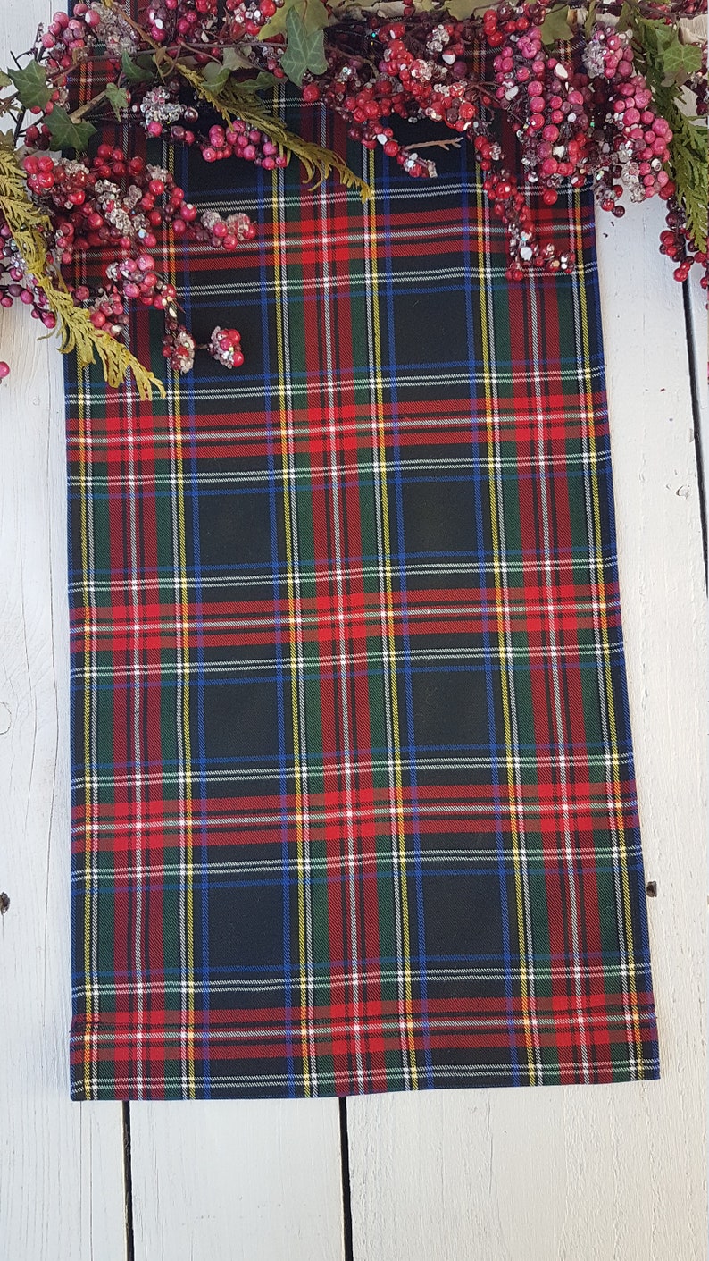 May include: Black and red plaid fabric with a green, white, and blue plaid pattern. The fabric is folded and lying on a white wooden surface.