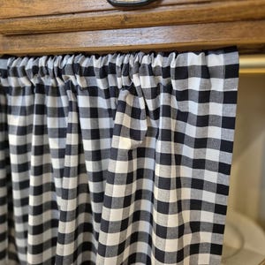 May include: Black and white checkered valance with a gathered top. The valance is hanging from a wooden cabinet.
