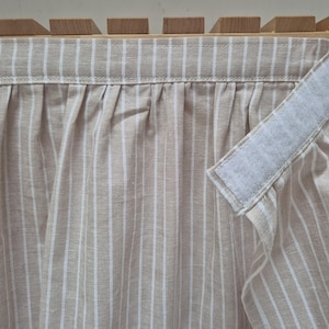 May include: A beige and white striped fabric curtain with a white velcro strip attached to the top edge.
