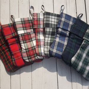 Könnte beinhalten: Sechs Weihnachtsstrümpfe aus kariertem Stoff in verschiedenen Farben, darunter Rot, Grün, Blau, Schwarz und Weiß. Die Strümpfe sind in einem Halbkreis auf einer weißen Holzoberfläche angeordnet.