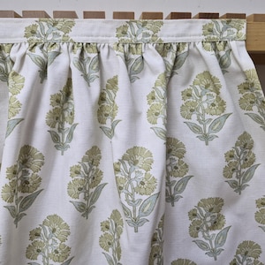 May include: White fabric with a repeating floral pattern in shades of green and gray. The fabric is gathered at the top, suggesting a curtain or valance. The floral design features stylized blooms and leaves.