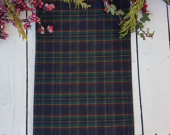 May include: A plaid table runner in shades of green, black, and red. The runner is on a white wooden surface.