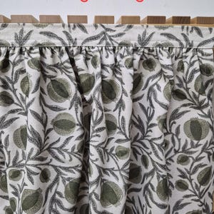 May include: Close-up of fabric with a pomegranate pattern in shades of green and gray on a white background. The fabric is draped, and the text "Pomegrante green" is visible in red at the top.