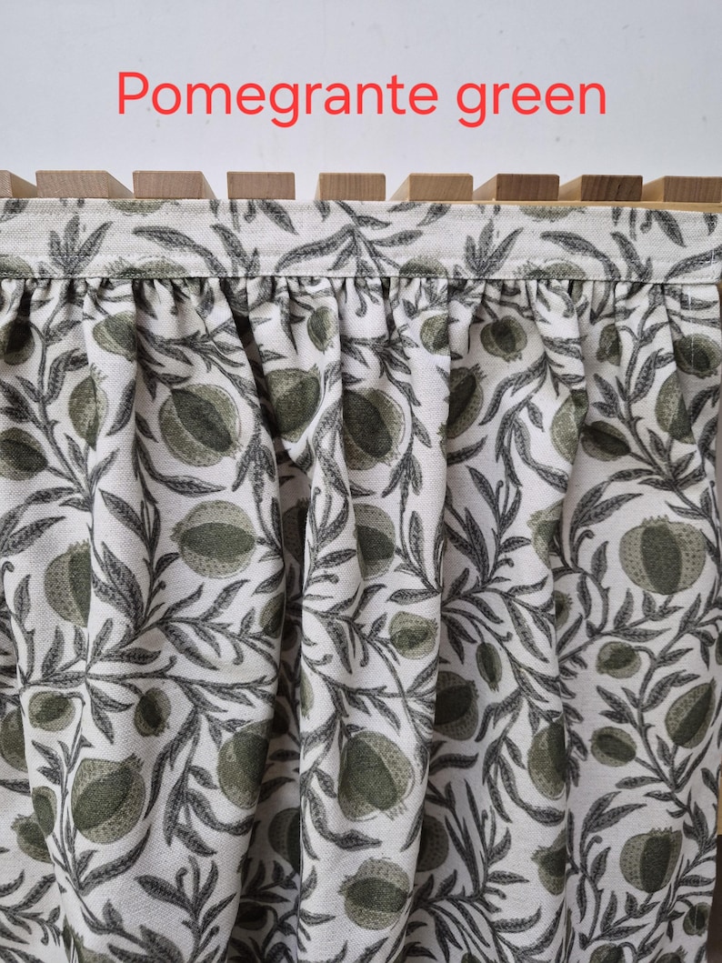 May include: Close-up of fabric with a pomegranate pattern in shades of green and gray on a white background. The fabric is draped, and the text "Pomegrante green" is visible in red at the top.