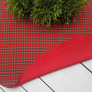 May include: Red and green plaid tablecloth with a solid red underside. The tablecloth is round and has a fringed edge.