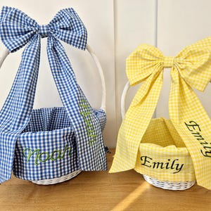 May include: Two white wicker baskets with blue and yellow gingham bows. The blue basket has the name "Noah" embroidered on it and the yellow basket has the name "Emily" embroidered on it.