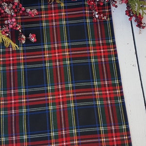 May include: Red, green, blue, and white plaid table runner with a black background. The runner is on a white wooden surface.