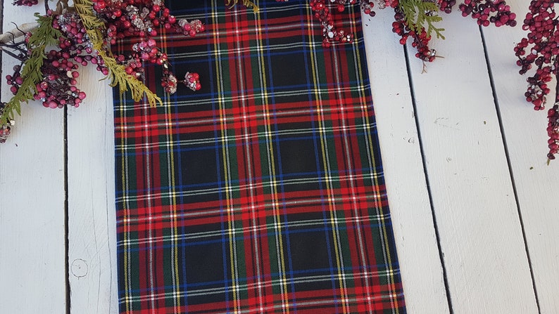 May include: Red, green, blue, and white plaid table runner with a black background. The runner is on a white wooden surface.
