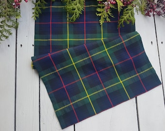 May include: A green, blue, yellow and red tartan table runner. The runner is folded in half and is lying on a white wooden surface.