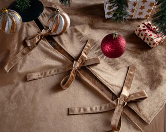 Puede incluir: Una falda de árbol de Navidad dorada con lazos de cinta adjuntos. La falda está rodeada de decoraciones navideñas, incluyendo adornos, regalos envueltos y una bola roja brillante.