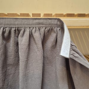 May include: A close-up of a gray fabric with a textured surface. The fabric is gathered at the top and has a white velcro strip attached. The fabric appears to be part of a curtain or similar textile.
