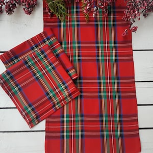 May include: Two red and green tartan napkins, one folded on top of the other, on a white wooden surface.