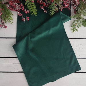 May include: A dark green velvet table runner on a white wooden surface. The runner is folded in half and has a subtle sheen.