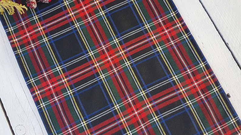 May include: Black and red plaid table runner with green, blue, and white accents. The runner is made of a woven fabric and has a subtle sheen.