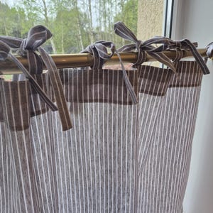 May include: White and brown striped curtains with brown trim and gray fabric ties hanging on a gold rod.