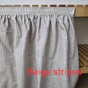 May include: Beige and white striped fabric curtain with the text "Beige stripes". The curtain is hanging from a wooden shelf. The fabric has a vertical stripe pattern.