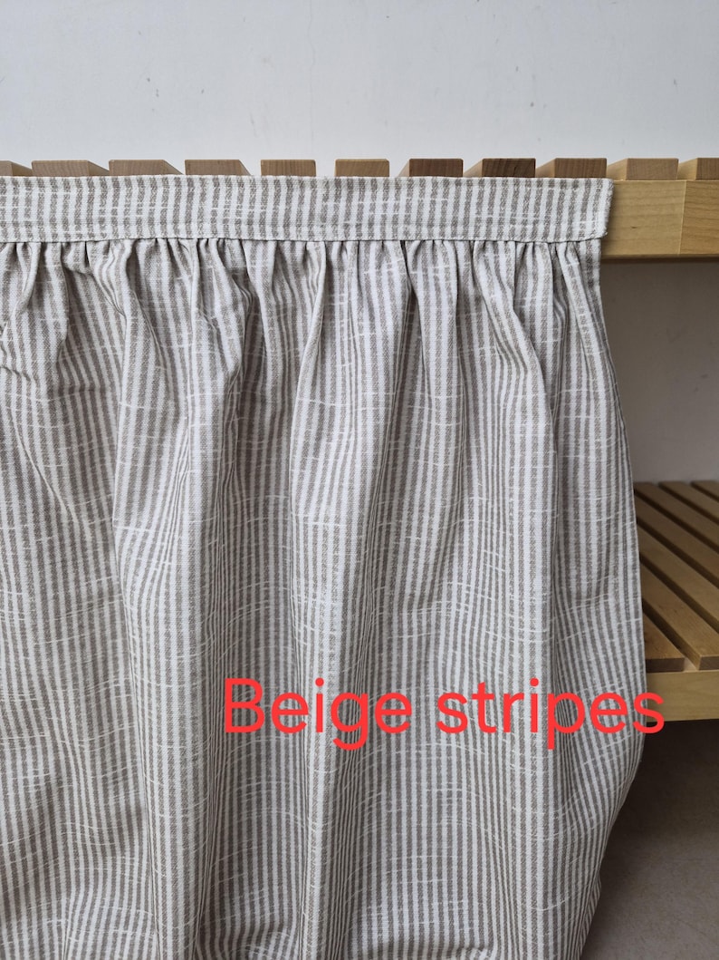 May include: Beige and white striped fabric curtain with the text "Beige stripes". The curtain is hanging from a wooden shelf. The fabric has a vertical stripe pattern.