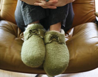 Puede incluir: Una persona con jeans azules y pantuflas de peluche verde se sienta en un sillón de cuero marrón.