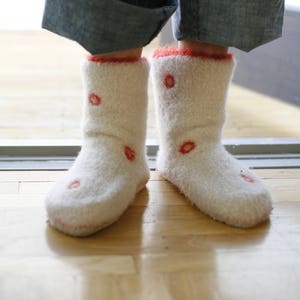 Puede incluir: Un par de calcetines blancos y peludos con diseños de flores rojas. Los calcetines están enrollados en la parte superior y los lleva alguien que lleva pantalones vaqueros azules.