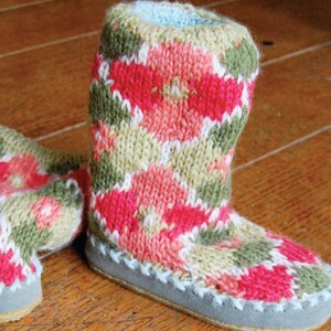 Op de afbeelding: Een paar gebreide pantoffels met een bloemenpatroon in tinten roze, groen en wit. De pantoffels hebben een lichtblauwe suède zool.