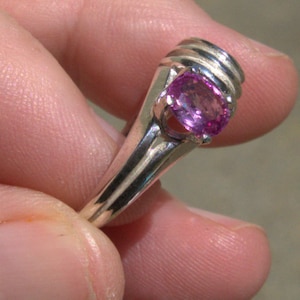May include: A silver ring with a pink gemstone set in a prong setting. The ring has a textured band.