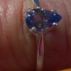 May include: A silver ring with a pear-shaped purple gemstone.