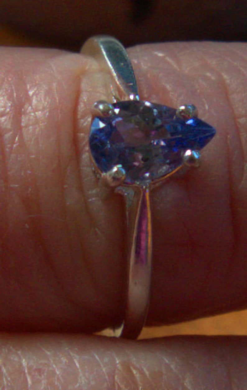 May include: A silver ring with a pear-shaped purple gemstone.
