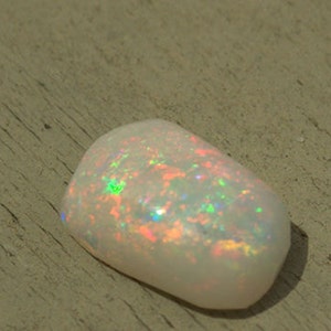 May include: A white opal gemstone with iridescent rainbow colors. The opal is a smooth, oval shape and has a natural, organic look.