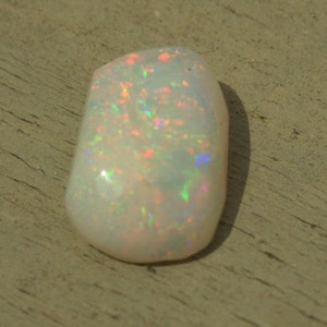 May include: A white opal gemstone with iridescent flashes of color, including pink, green, and blue.