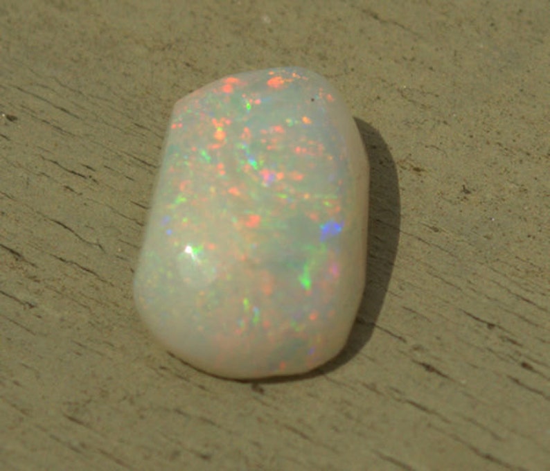 May include: A white opal gemstone with iridescent flashes of color, including pink, green, and blue.