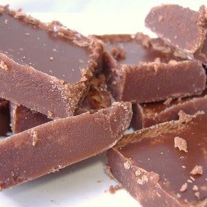 May include: A collection of thick, rectangular pieces of brown chocolate fudge. The pieces have a smooth, glossy top surface and a dense, textured appearance along the sides, with small, crumbly fragments scattered around the edges of each block.