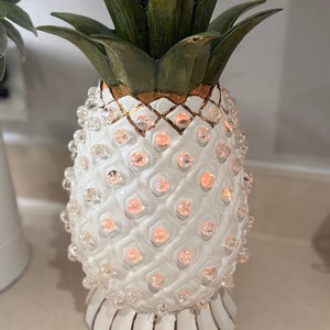 May include: White ceramic pineapple lamp with a gold trim and green leaves. The pineapple is covered in small, clear glass beads.