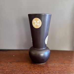 May include: A dark brown ceramic vase with a rounded base and a flared top. The vase is decorated with white and gold geometric patterns.