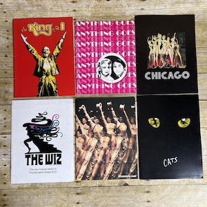 May include: A collection of six vintage musical theater playbills. Titles include "The King and I," "Anything Goes," "Chicago," "The Wiz," "A Chorus Line," and "Cats." The playbills feature colorful graphics and text.