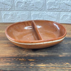 May include: A brown, oval-shaped divided serving dish with a white stripe around the rim. The dish is made of ceramic and has a glossy finish. The dish is designed to hold two different types of food.