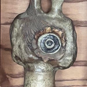 May include: A ceramic vase with a unique, abstract design. The vase has two openings and a textured surface with a circular, brown and black design on the front.