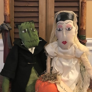 May include: Handmade Halloween dolls of Frankenstein and his bride, with an orange pumpkin. Frankenstein is green with black hair and a black coat. The bride wears a white dress and veil. The pumpkin has a tag that says "Made for each other."