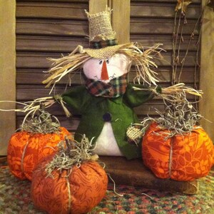 Primitive Country Fall Scarecrow in pumpkin patch with three pumpkins