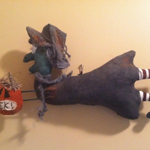 May include: A Halloween decoration featuring a witch riding a broom. The witch has a green face, gray hat and dress, and striped legs. She carries an orange pumpkin with the word "EEK!" on it.