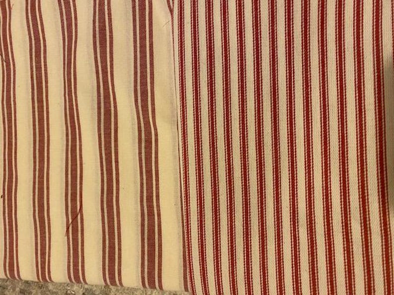 May include: Close-up of two fabric swatches with vertical stripes. One swatch features wide, burgundy stripes on a cream background. The other has narrower, red stripes on a cream background. The fabrics appear to be cotton or linen, suitable for home decor.