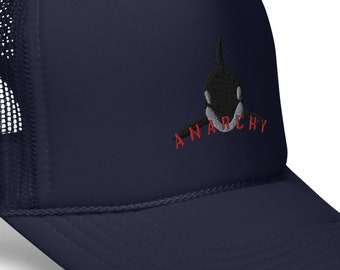 May include: A navy blue trucker hat with a black and white orca graphic and the word "ANARCHY" in red embroidered on the front.