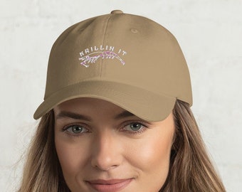 May include: A tan baseball cap with an embroidered alligator and the text "Krillin It" in white.