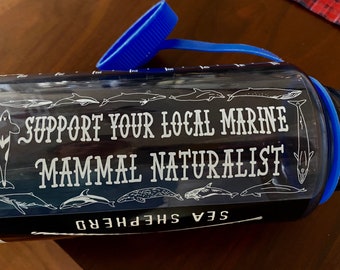 May include: A black water bottle with a white sticker that says "Support Your Local Marine Mammal Naturalist" and a white silhouette of a whale. The sticker is surrounded by a row of white whale silhouettes. The bottle has a blue lid.