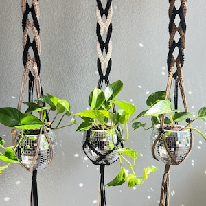 May include: Three macrame plant hangers with black and white, black and beige, and brown and black cords. Each hanger has a disco ball planter with a green plant inside.