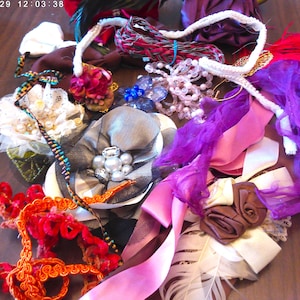 May include: A collection of craft supplies including ribbons, fabric flowers, and beaded accents in various colors. The assortment features shades of red, pink, purple, white, and gray, with textures like tulle, satin, and lace. A variety of embellishments for crafting and design.