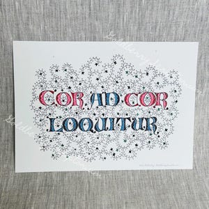 May include: A white rectangular print featuring the Latin text COR AD COR LOQUITUR in stylized black, red, and blue lettering. The text is surrounded by an intricate, hand-drawn pattern of fine black vines with small green and black leaves.