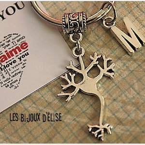 Könnte beinhalten: Silberner Schlüsselanhänger mit einem Anhänger eines Neurons, einem Buchstaben M Anhänger und einem kleinen Anhänger mit der Aufschrift "LES BIJOUX D'ELISE" und einem Herz mit dem Wort "J'aime" in Rot, umgeben von dem Wort "love you" in verschiedenen Sprachen.