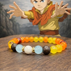 May include: A beaded bracelet with a gradient of orange, yellow, and brown beads. The bracelet features a mix of colors and textures, including light blue and white beads. The background includes a cartoon character.