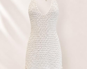 May include: A cream-colored crochet mini dress featuring a halter neckline with tie straps, a deep V-neck, and adjustable side drawstrings with small beads at the ends. The garment is crafted with a textured knit pattern throughout the bodice and skirt.